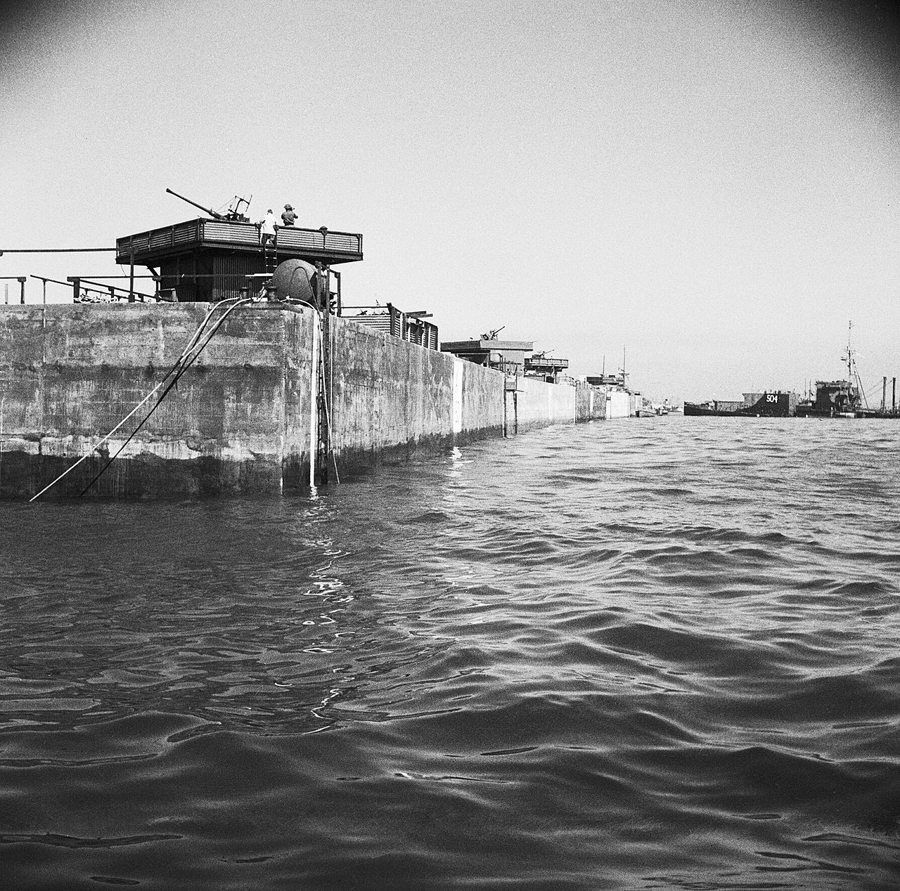 A line of Phoenix caisson units forming the breakwater of Mulberry Harbour at Arromanches, June 1944